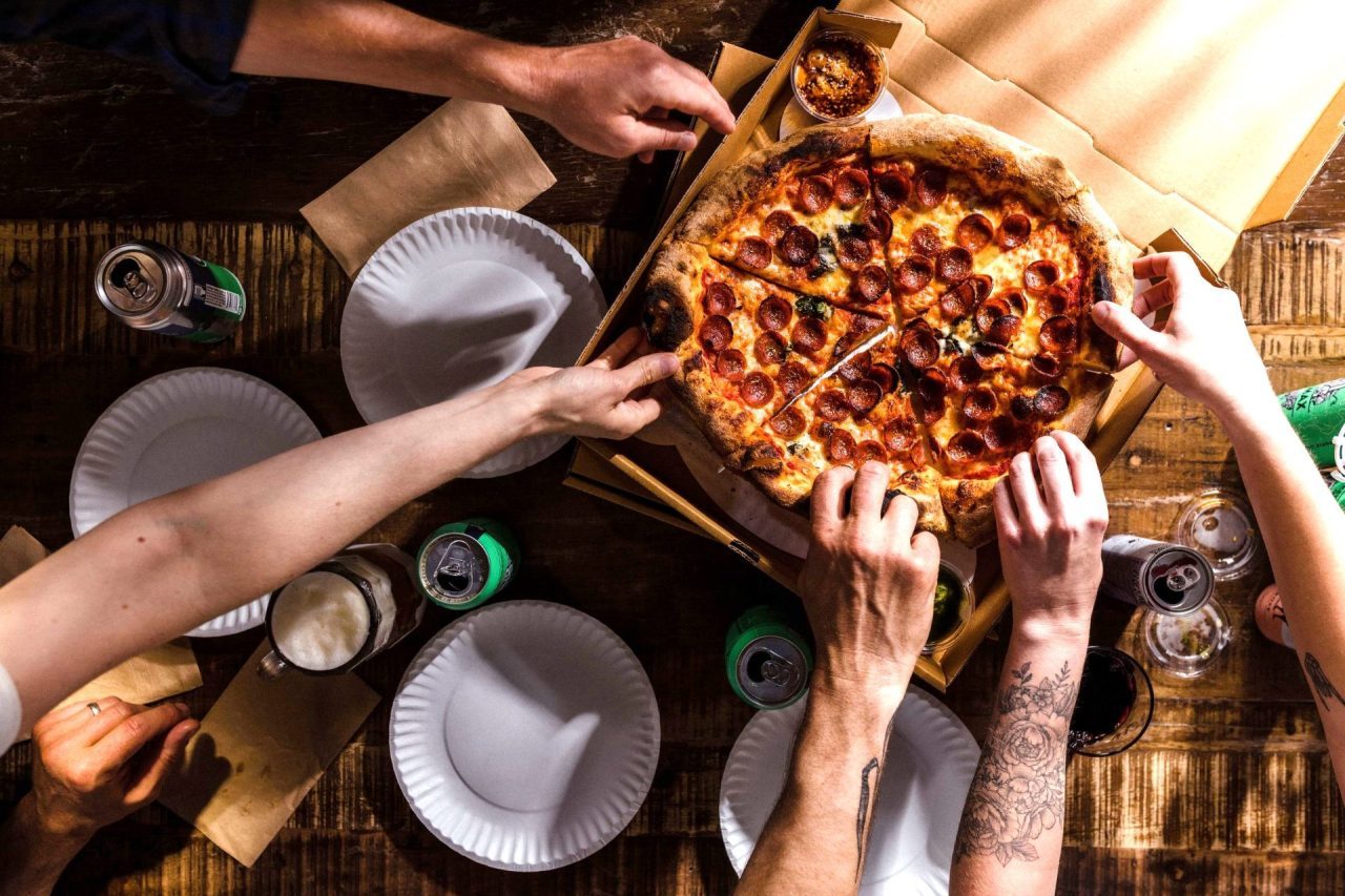 Several hands grabbing slices of pizza