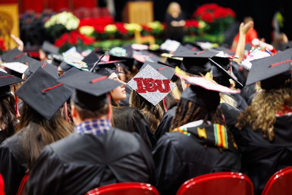 Students facing forward in black gowns wearing black graduation caps with red tassels